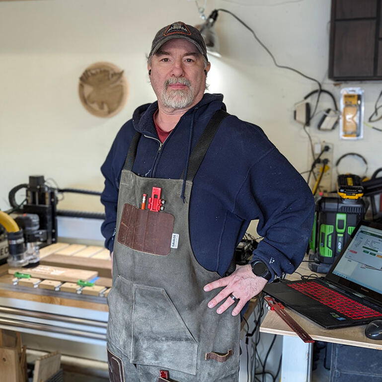 A picture of a man, wearing a canvas apron and tools in the background.